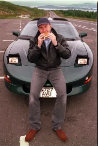 COMEDIAN Fred MacAulay WITH SUPER CAR TRANS AM EATING A HAMBURGER