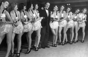 Comedian Tommy Handley stands with a line up of modern girl secretaries at Jack