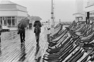 Deckchairs Prints: A couple walk along the deserted pier in Blackpool as the rain arrives to interrupt a