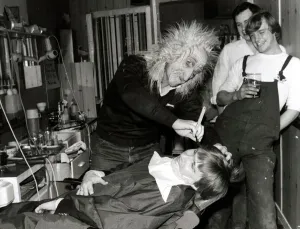 00186 Prints: A customer sits in the barbers chair having his faced shaved by a man in a mask at Steve