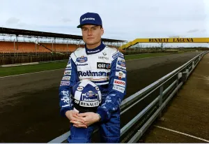 David Coulthard sitting on fence at race track holding helmet Formula One racing