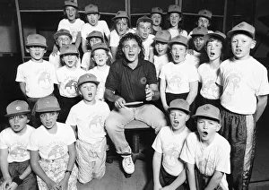 David Essex Singer surrounded by choir of school children wearing baseball caps