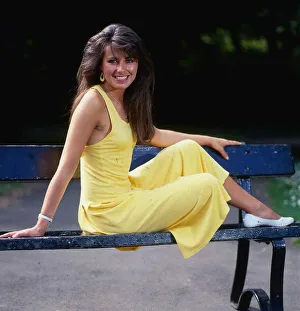 Debbie Greenwood TV presenter July 1987 sitting o a bench wearing a yellow dress