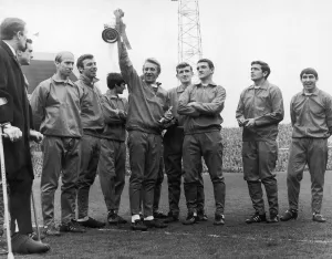 Track Suit Prints: Dennis Law holds the division one championship trophy at Old Trafford with his fellow