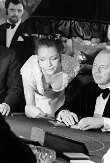 00161 Collection: Diana Rigg in a low cut dress leans across the Black Jack table in a casino showing off
