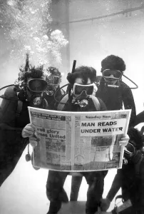 00079 Prints: Divers while away some time reading their local newspaper on a charity dive