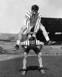Dunfermline football player Bert Paton leap frogs teammate Alex Ferguson during a