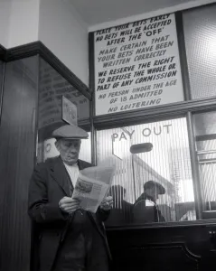 00170 Prints: An elderly man studies the form guide inside A E Fane and Co betting shop in Islington