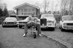 Elton John pictured at his home, sitting on a small motorbike in front of four of his