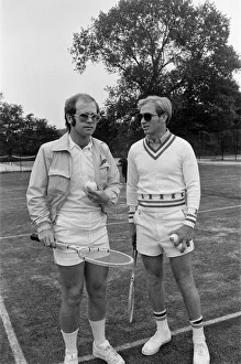 Elton John plays tennis against Larry King on an outer court at Wimbledon. 25th June 1974