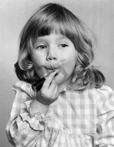 Cosmetics Prints: Emma Varsanyi. March 1976 P034769 Little girl putting on lipstick