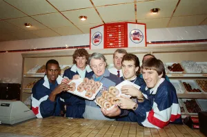 Shellsuit Prints: England manager Bobby Robson enjoying a selection of doughnuts with members of his