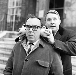 Eric Morecambe gets a new style in ear muffs with coffee cups from his partner