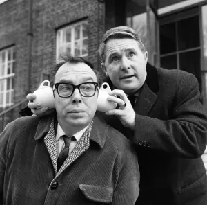 Eric Morecambe gets a new style in ear muffs with coffee cups from his partner