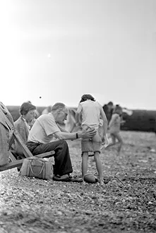 Waves Prints: Family help a young boy to get changed as they sit on their deckchairs on the beach