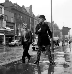 Fashion: Clothing. Unisex clothes. A girl wears a bowler hat, dark overcoat, pin stripes
