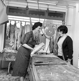 Customer Prints: A female butcher seen here at work in her shop, serving a customer at the counter. 1963