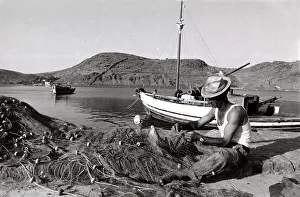 Fisherman Prints: fisherman tends to his nets in Greece - fishing boat mountains river