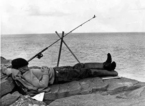 00089 Prints: Fishing - A fisherman takes a nap whilst fishing of some rocks - South Wales - 24th July