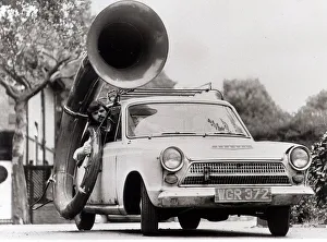 Novelty Vehicle Prints: Ford Cortina Mk1 Car. A man drives the car with a large horn instrument strapped to
