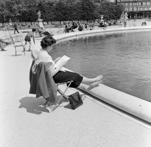 France Paris - A lady sits resting her feet beside a pond in a park reading a letter