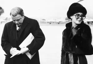 Frank Sinatra Actor and Singer writing on a piece of paper while standing at an airport