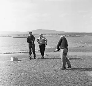 Trolley Prints: Three friends tee off for a round of golf on a very windy Fort Island Golf links Hotel