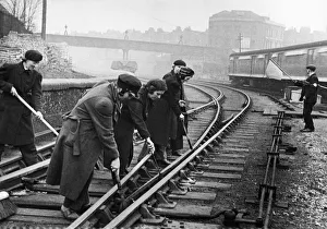 A gang of length women at work oiling and scraping at Westbourne Park Railway Station