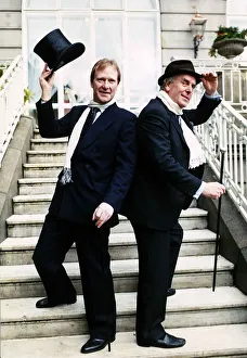 00141 Prints: George Cole actor and Dennis Waterman standing on doorsteps raising a top hat and cane