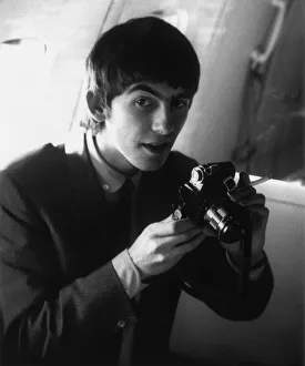 George Harrison holding his camera on board the plane en route to New York, USA