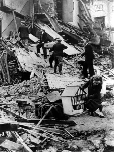 War And Prints: A girl has rescued a dolls house from the destruction of a house as salvage workers sift