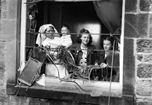 Girls and a nurse holding a litte baby looking out through the smashed window of a bomb