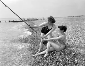 Swimsuit Prints: Two girls try a spot of fishing during a visit to the beach in Springtime Britain