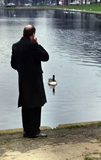 Relaxation Prints: Gorden Kaye actor looking out over a boating lake in a park with duck paddling towards