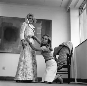 Kneeling Prints: Graziella Fontana fashion June 1965 A model is helped into a long coat with large