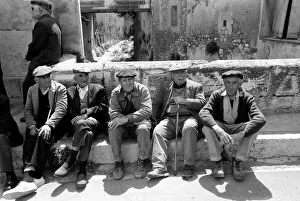 Walking Stick Prints: A group of pensioners sitting down against a wall on a street in a French village