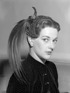 1950s Fashion Prints: Hat Fashion by Norman Hartnell Wearing a feathered hat looking uncertain and stiff