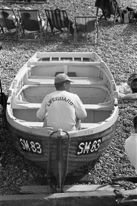 East Sussex Prints: Holiday scenes at Brighton. Lifeguard sitting in a rowing boat on Brighton beach
