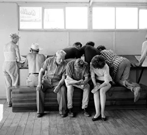 00170 Prints: Holidaymakers study the form guide at a betting shop in the form of a wooden chalet