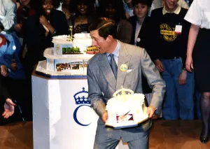 HRH Prince Charles about to throw a birthday cake to a crowd of onlookers during his
