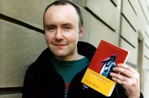 Irvine Welsh author wearing blue fleece jacket green T shirt holding copy of his book
