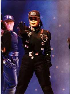 Janet Jackson on stage right arm outstretched wearing baseball cap performing