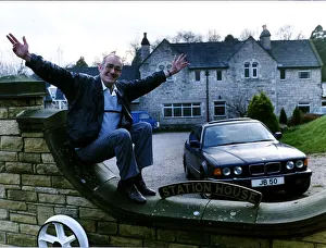 Jim Bowen comedian / TV presenter sitting on his garden wall with arms outstretched