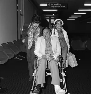 Wheelchair Prints: Joan Collins with husband Ron Kass and daughter Katyana arriving at Heathrow from Los