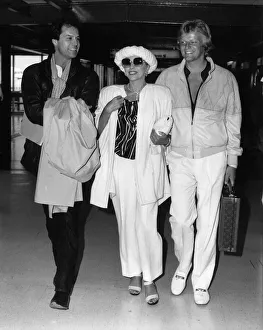 Joan Collins walking through Heathrow Airport with her boyfriend Peter Holm on her left