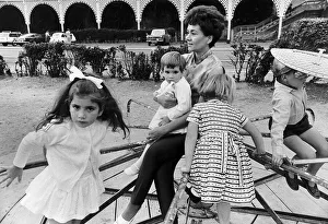 Joan Plowright Actress sitting on merry go round holding child with other children