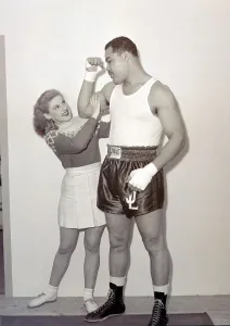 1948 Prints: Joe Louis with female model cheerleader feeling the size of his bicep at Earls Court