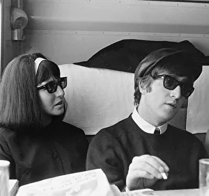 John Lennon and Cynthia Lennon wearing a dark wig over her blonde hair sitting on a train
