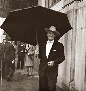 Core26 Prints: John Wayne standing under a big black umbrella in the rain in London October 1960