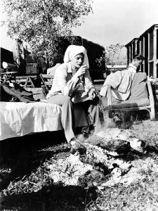 Katharine Hepburn wearing a towel around head sitting by an open fire drinking coffee